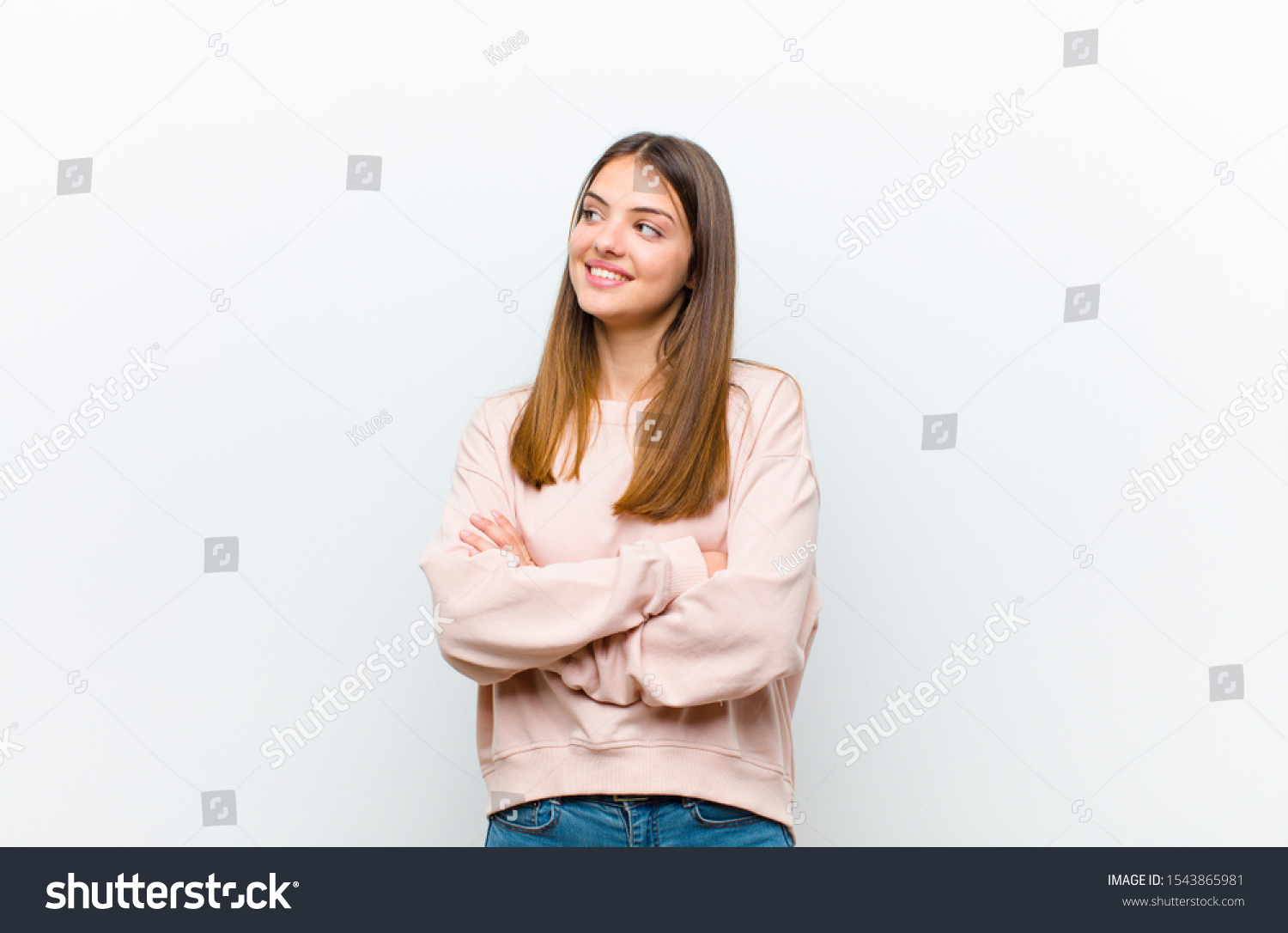 young pretty woman feeling happy, proud and hopeful, wondering or thinking, looking up to copy space with crossed arms against white background #1543865981
