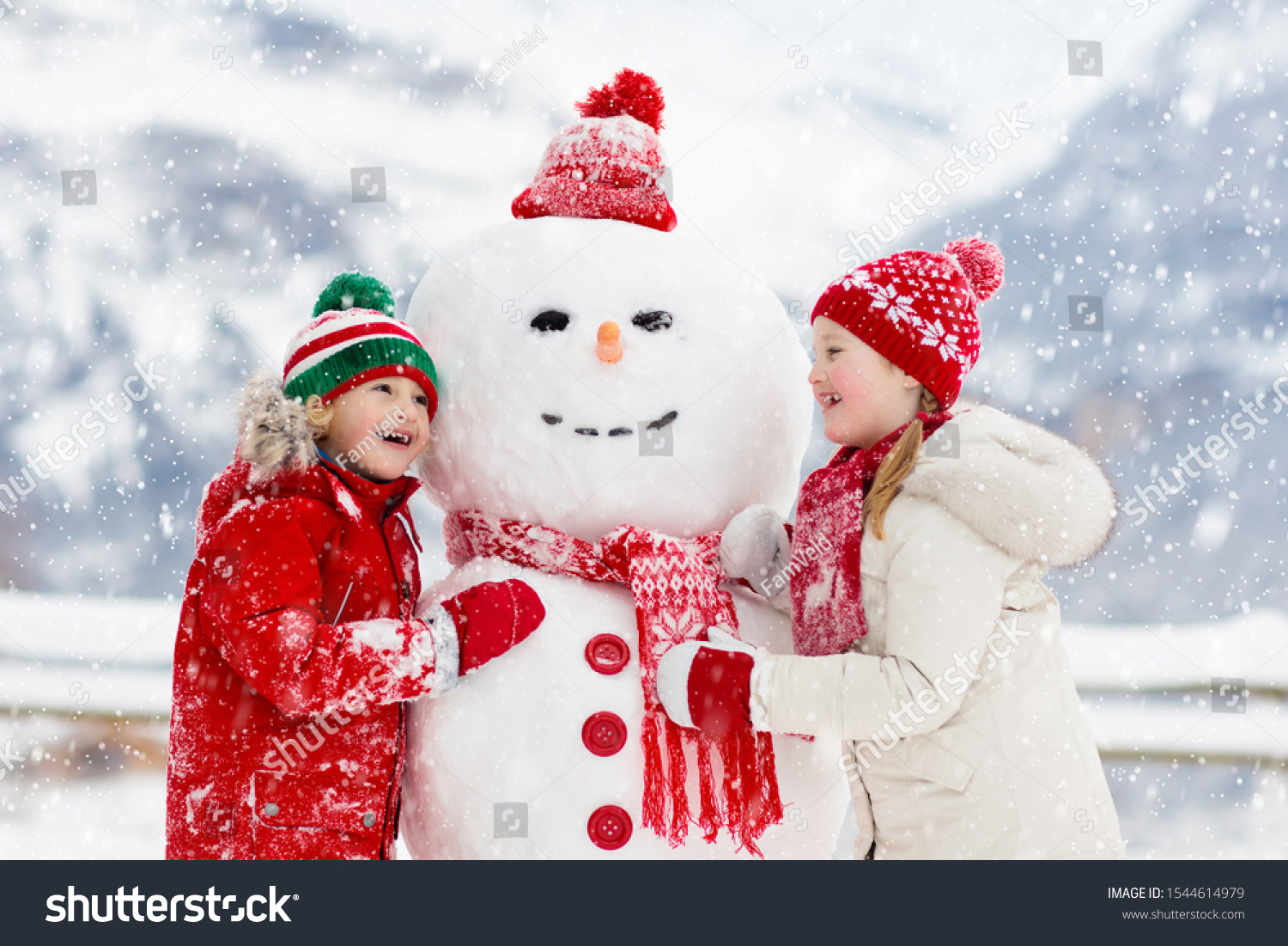 Child building snowman. Kids build snow man. Boy and girl playing outdoors on snowy winter day. Outdoor family fun on Christmas vacation in the mountains. Children play in Swiss mountain landscape. #1544614979