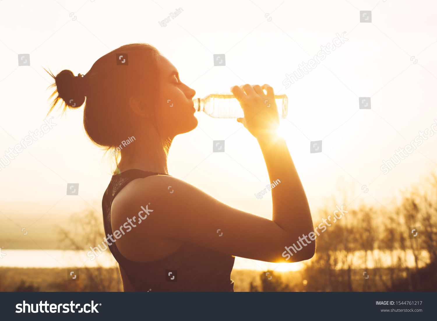 Beautiful girl in sportswear drinks water from a bottle at sunset #1544761217