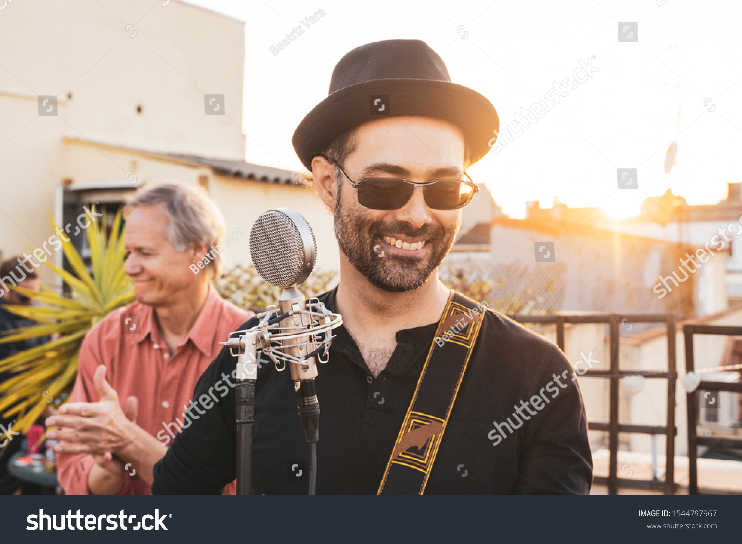 Man in adult age performing on a rooftop at summer season. Music live concerts concept. Lead singer of a rock band singing a song. Portrait of a hipster male musician playing on an intimate concert. #1544797967