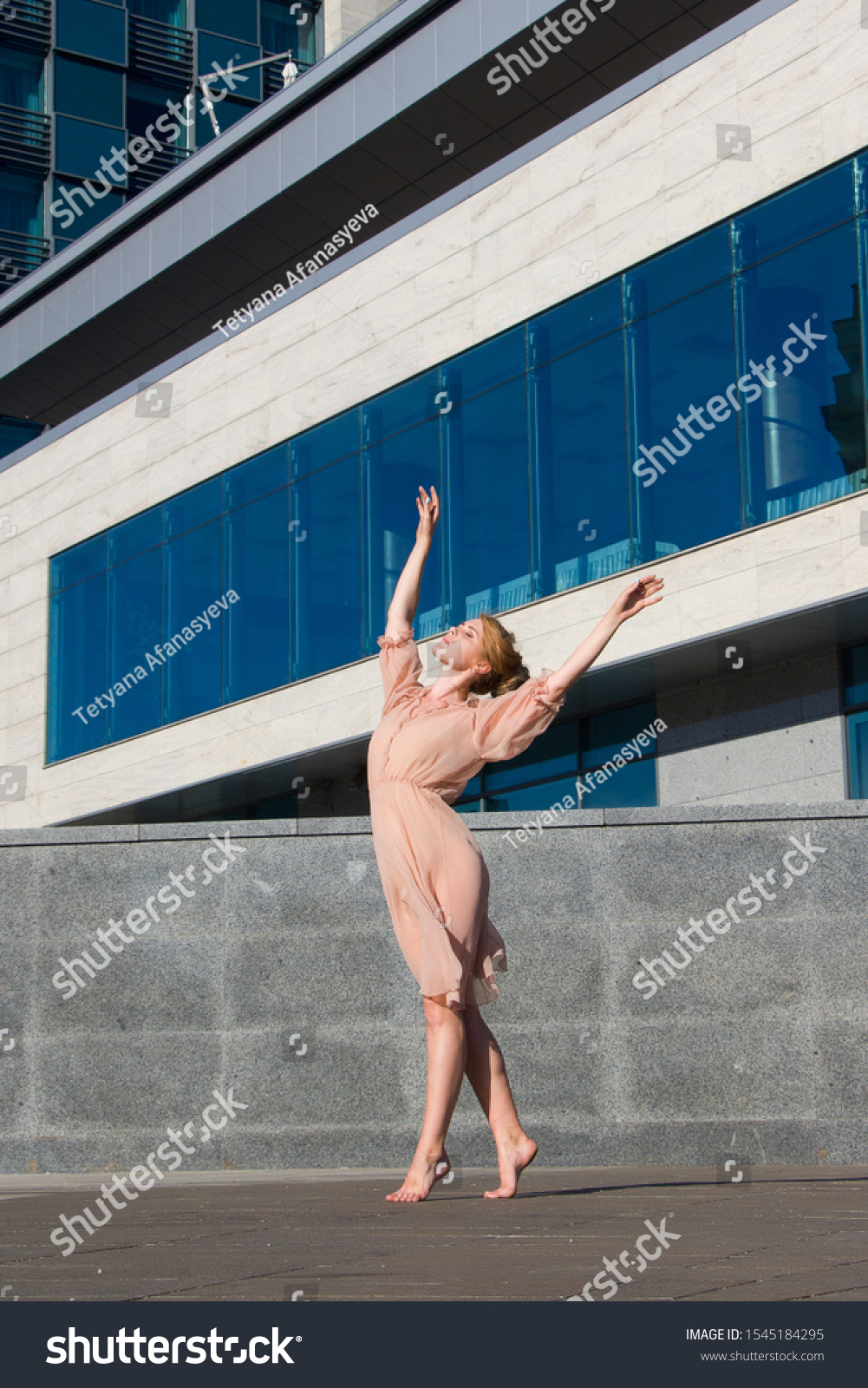 Ballerina in light dresses dancing on a street background of a modern glass building business center #1545184295