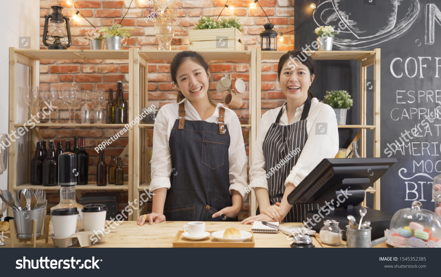Portrait of cheerful asian female barista laughing during working break together with positive smile. Partnership of youg women in common business cafeteria. two girl staff face camera in coffee shop #1545352385