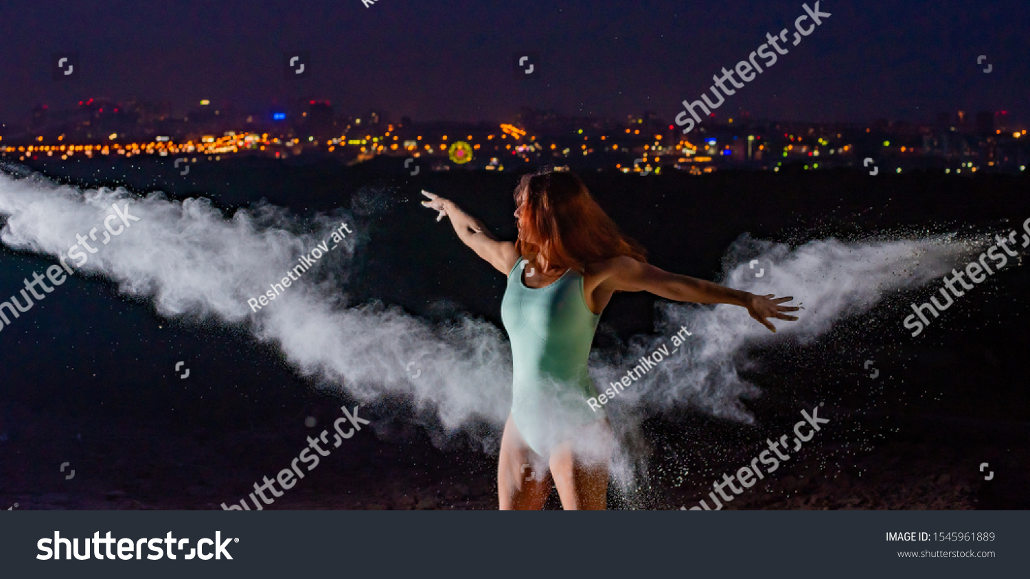 Red-haired woman in a blue bodysuit dancing in clouds of flour. A girl on the river bank jumping scattering white powder. #1545961889