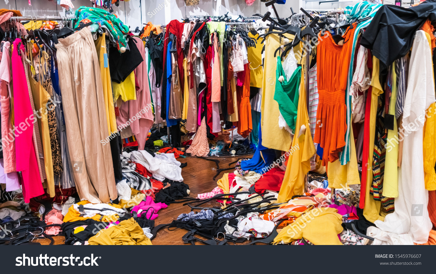 Messy clearance section in a clothing store, with colorful garments on racks and on the floor; fast fashion concept #1545976607