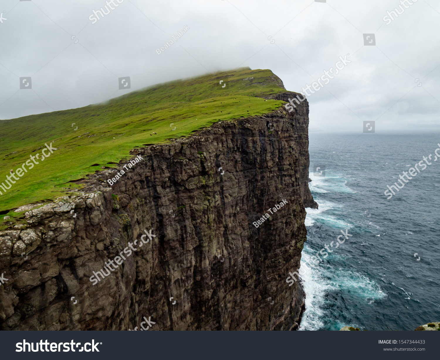 Steep cliffs of Faroe Islands. Green grass at the top, Ocean below the cliffs.  #1547344433