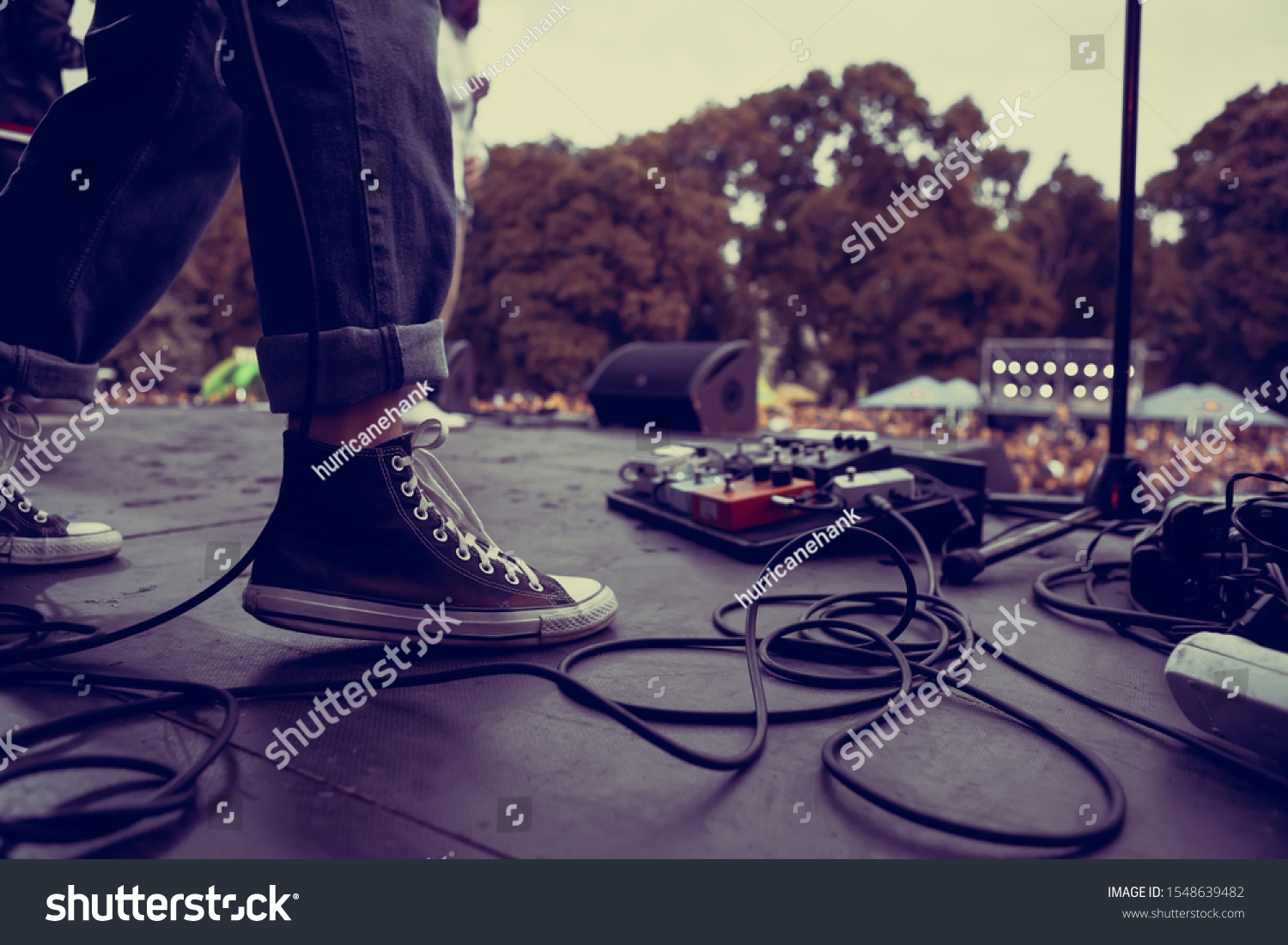 Guitarist perfroming live on hardrock concert stage outdoor.Feet of bass guitar player playing solo part on rock festival in summer.Punk band perform on scene,focus on old dirty sneakers of musician #1548639482