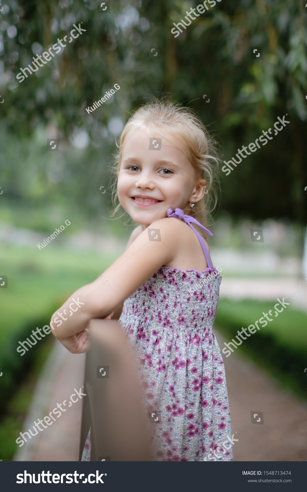A portrait of a cute little girl who laughs and laughs happily in the park on a warm summer day. Concept of summer holidays at sea and live style #1548713474
