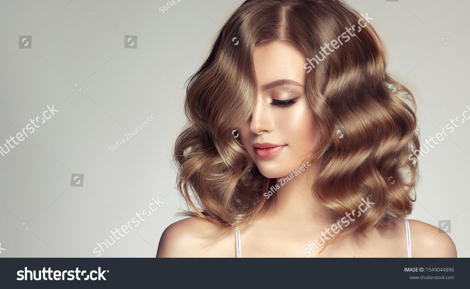 Woman with curly beautiful hair  on gray background. Girl with beauty a pleasant smile. Short wavy  hairstyle #1549044896