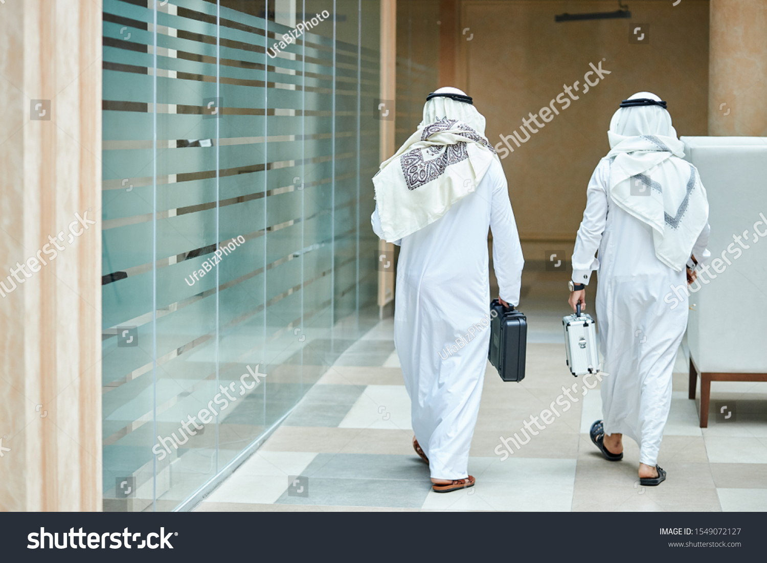 Rear view on sheikh businessmen holding case of money, going to meeting negotiations. In business center #1549072127