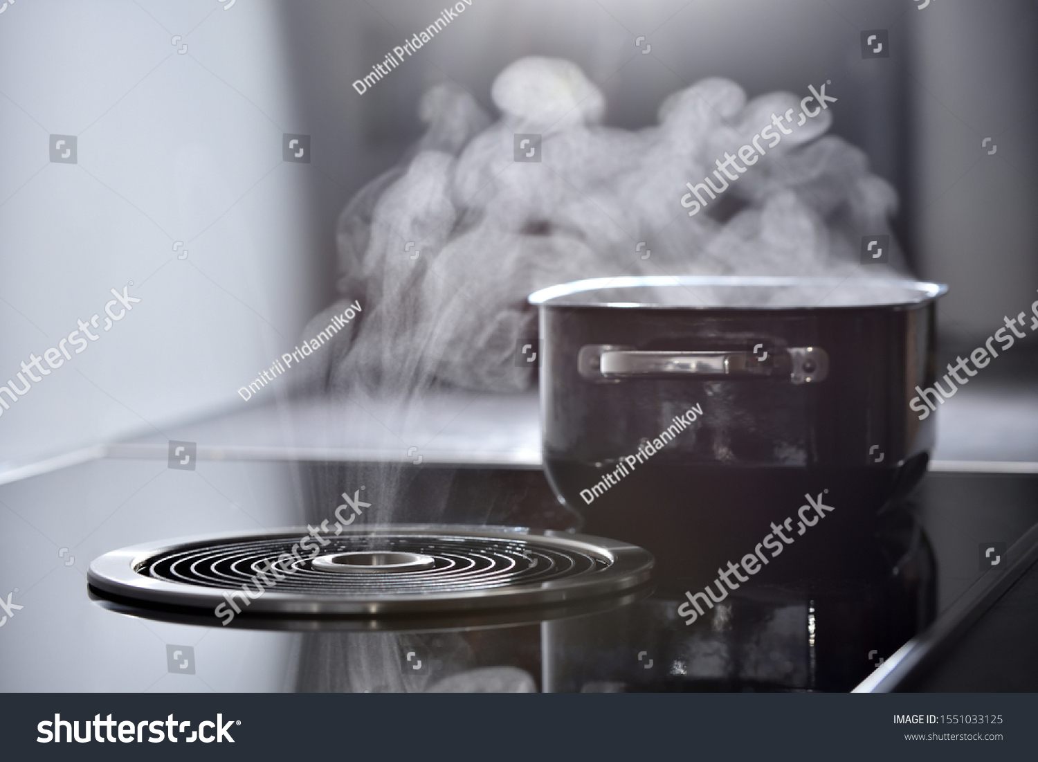Modern electric induction cooker with built-in ventilation and extractor hood which draws steam from boiling water in a pan. Steam from a boiling pot is drawn into the integrated range hood #1551033125