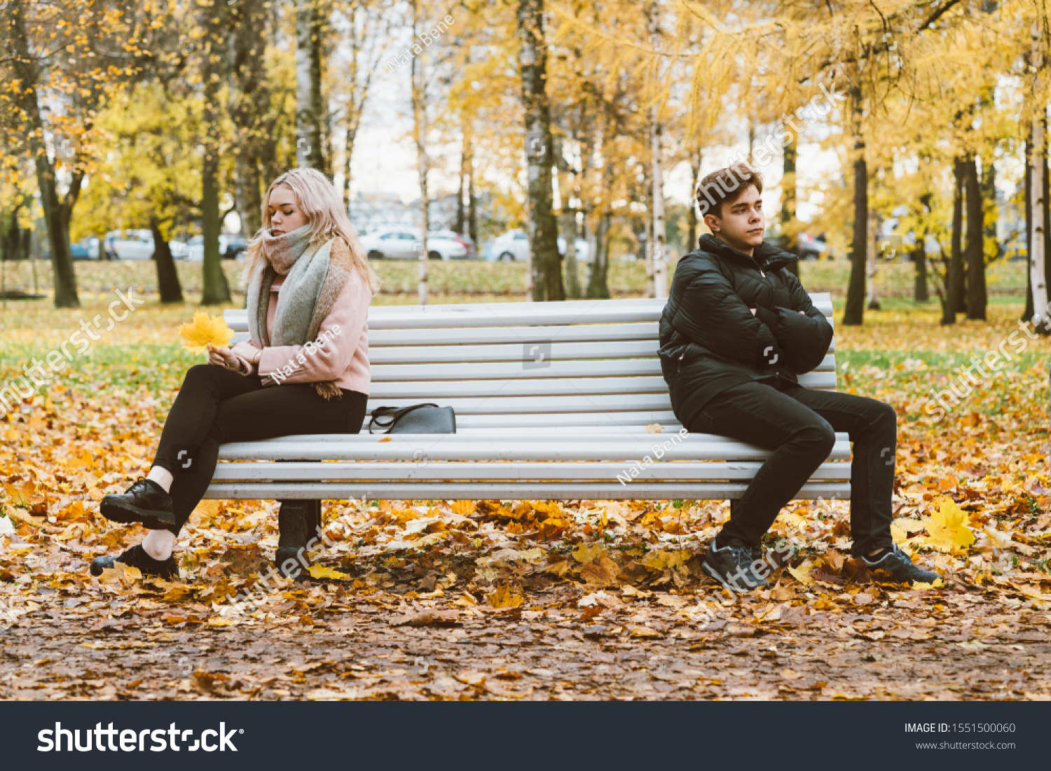 Two teenagers in love in a quarrel. A brunette boy and a blonde girl are sitting on opposite ends of the benches, their backs to each other, do not want to talk and talk. Teenage Difficulty Concept #1551500060