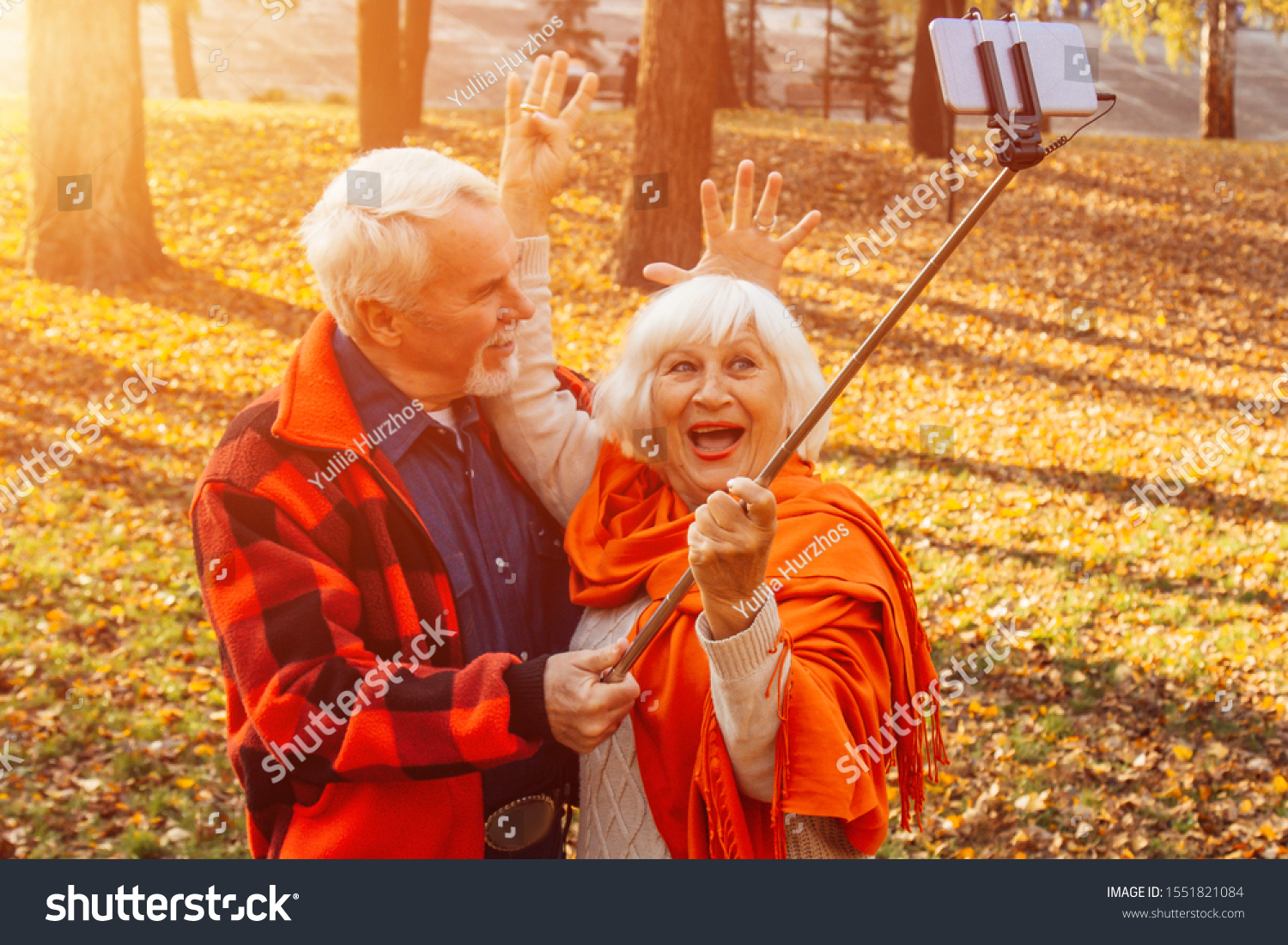 Positive mature couple showing tongues, laughing and fooling around while taking selfie pictures in the park #1551821084