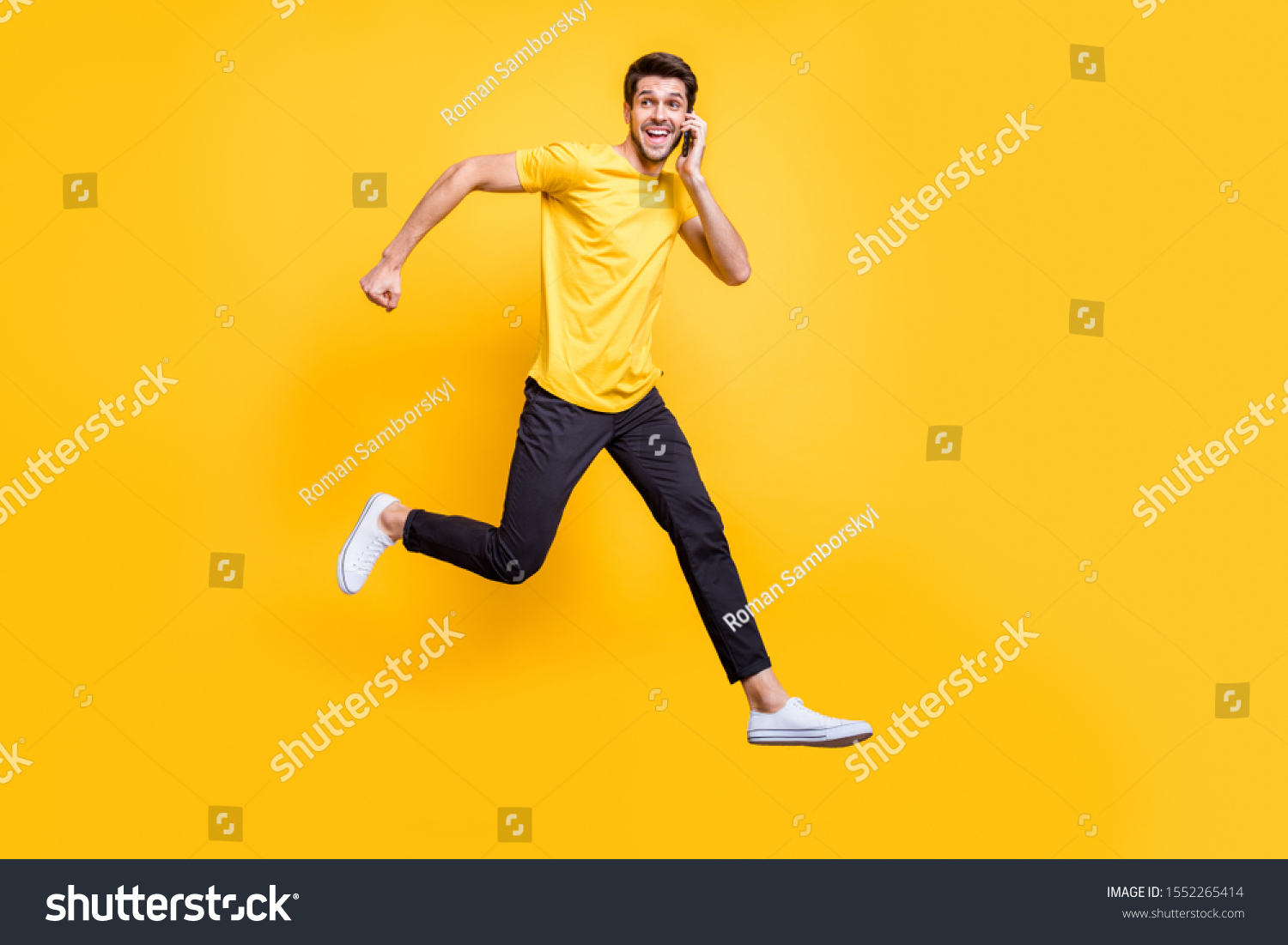 Full body photo of handsome guy jumping high talking telephone rushing romantic date see girlfriend wear casual t-shirt trousers isolated yellow color background #1552265414