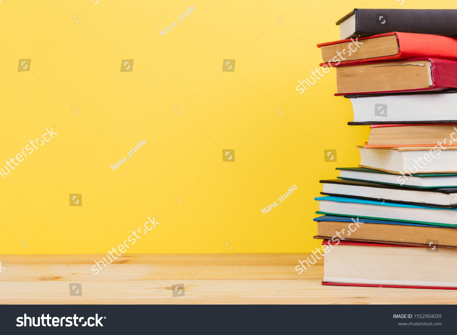 Simple Simple composition of many hardback books, unprocessed books on a wooden table and a yellow background. back to school. Copy space. Education. #1552904039