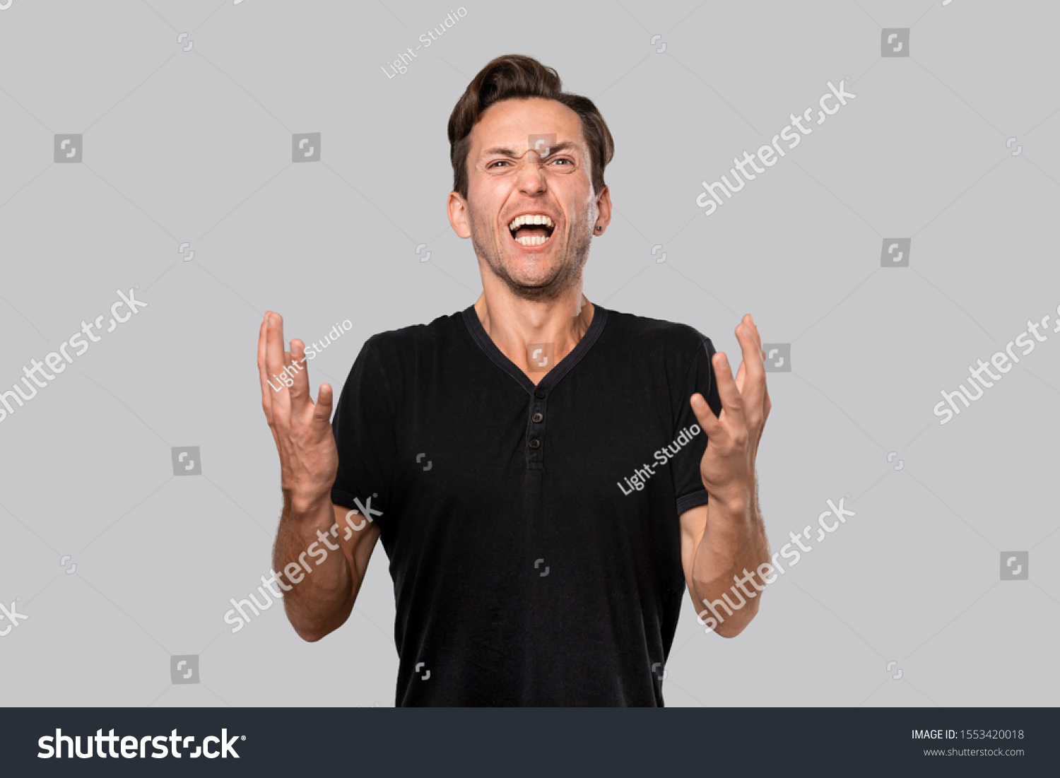 Angry man in a black tee shouting isolated over grey background. Concept of stress. #1553420018