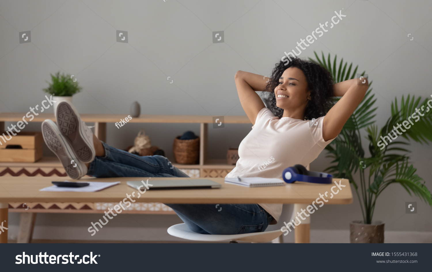 Satisfied African American woman relaxing at workplace with legs on table, happy female freelancer student dreaming, resting after work done in comfortable chair at home #1555431368