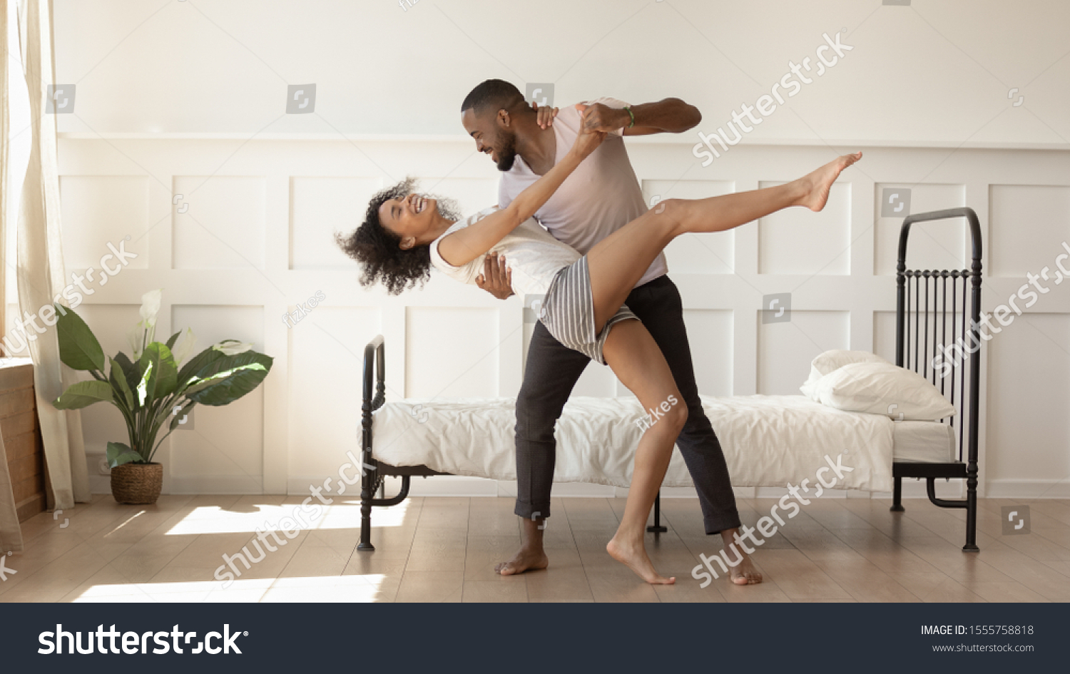 Excited african American millennial husband and wife dance swirl in bedroom, happy biracial mixed race dancer couple in pajamas have fun swaying together at home. Relocation, relationship goal concept #1555758818