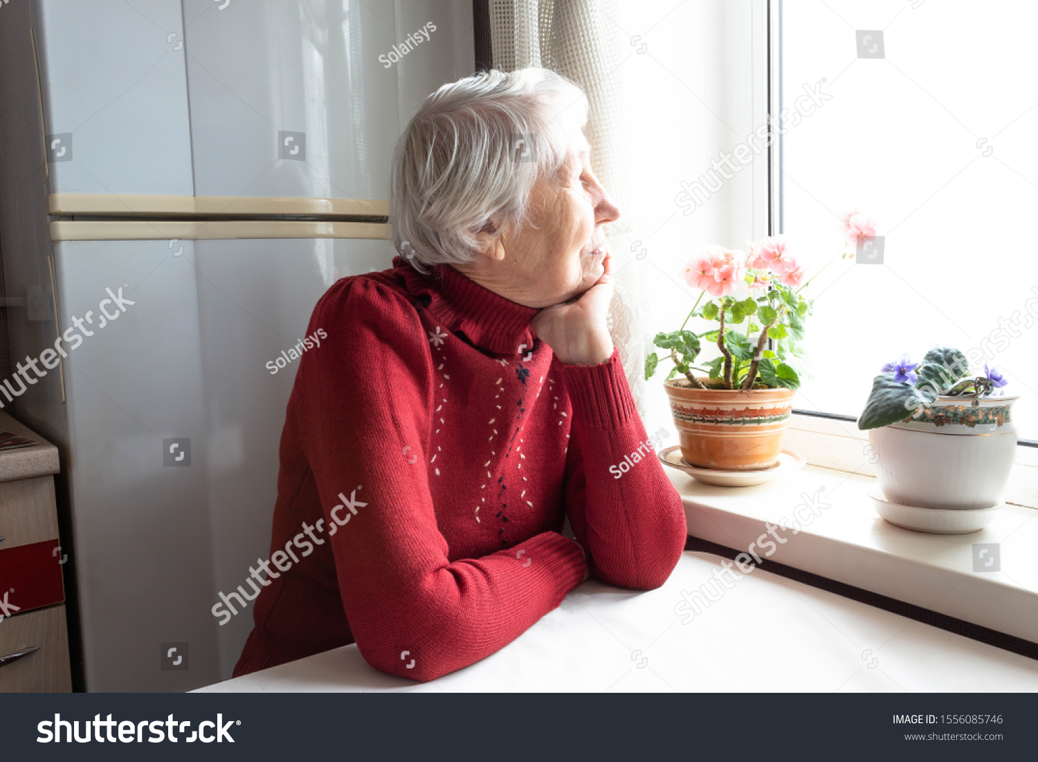 Old lonely woman sitting near the window at home. Concept of quarantine, coronavirus Covid-19. Danger for old people #1556085746
