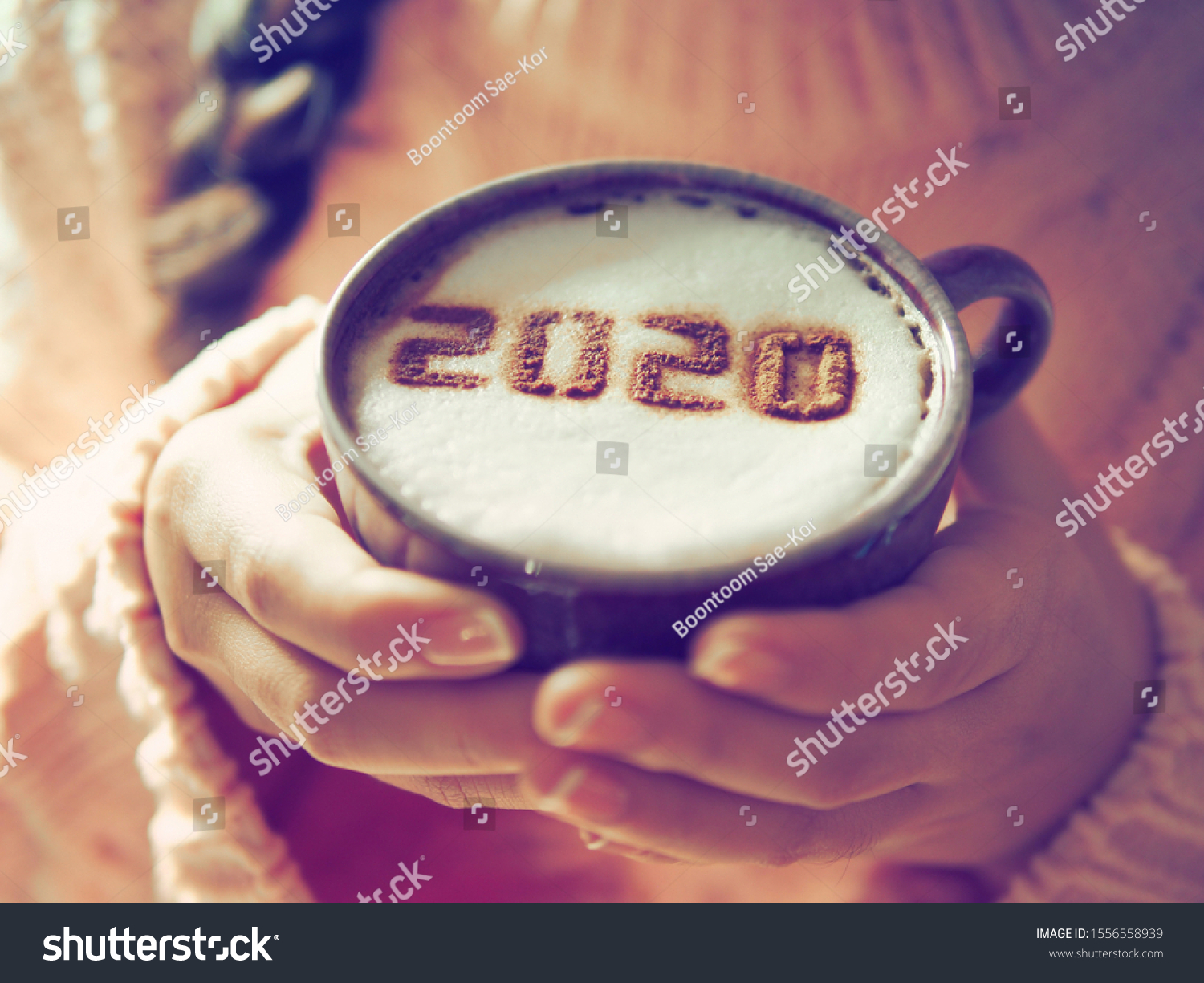 Number 2020 on frothy surface of cappuccino served in white cup holding by female hands with French nail polish. Food art creative concept for active days in New Year 2020. (close up, selective focus) #1556558939