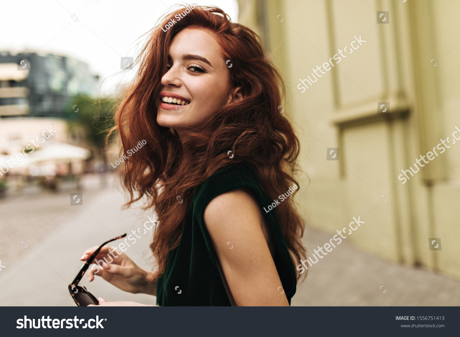 Attractive woman in dark green outfit smiling outside #1556751413
