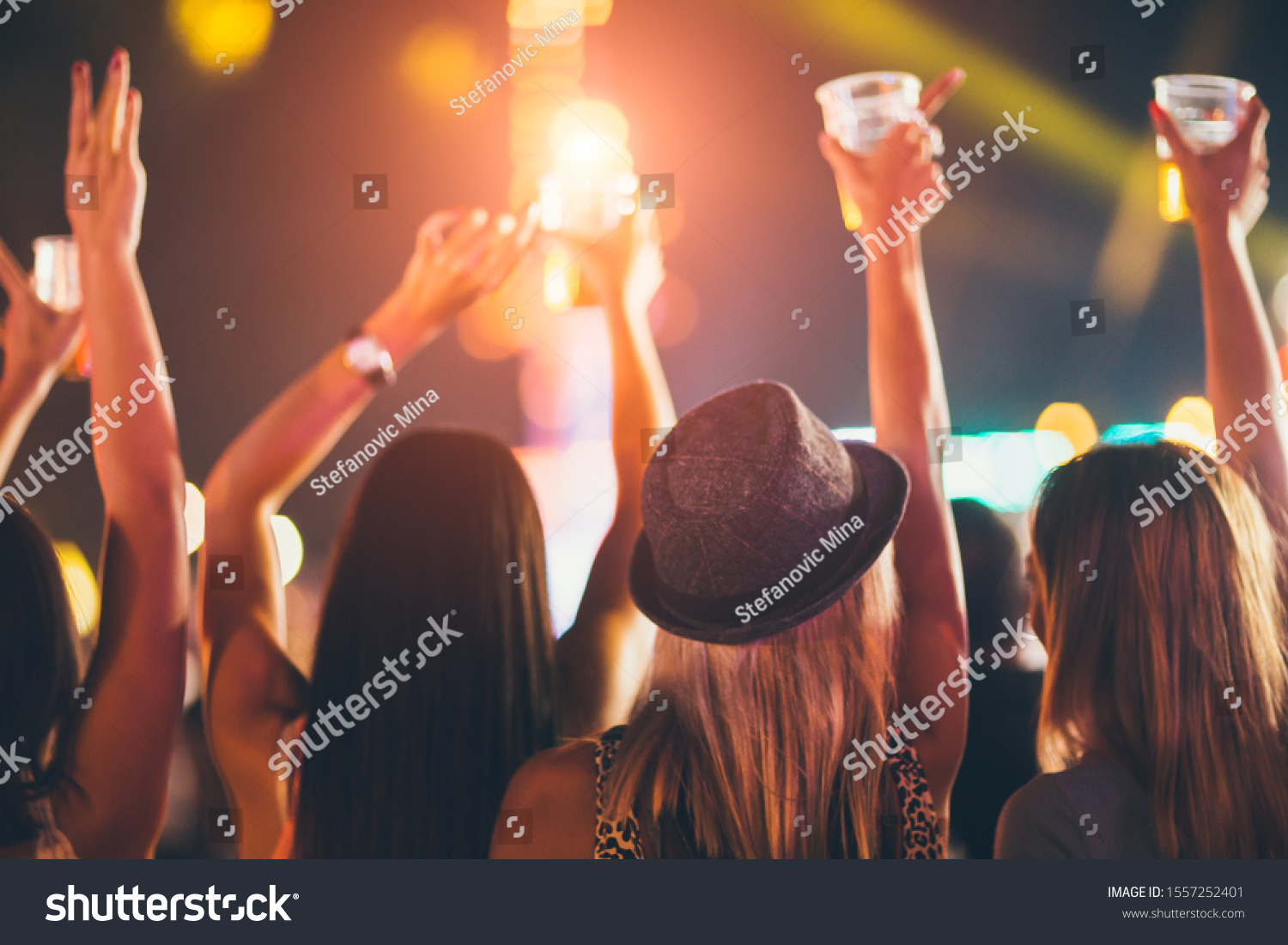 Back view of female friends drinking beer and dancing at music festival #1557252401