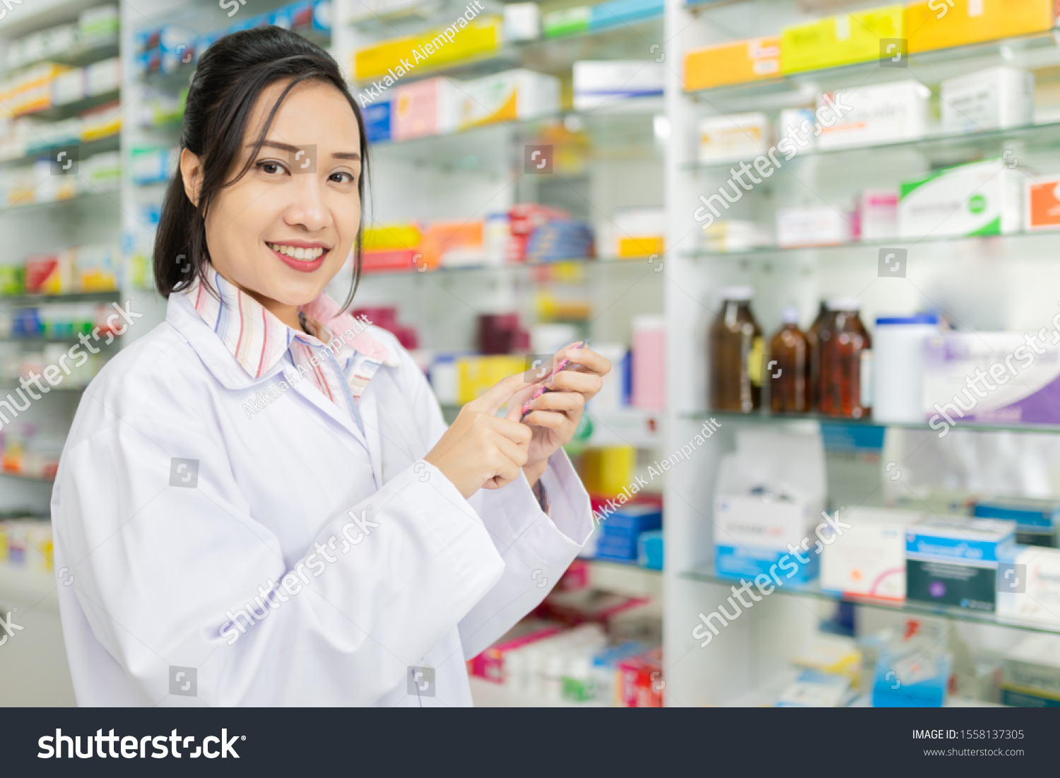 asian pharmacist standing in drugstore, they feeling happy and smile, pharmacist  female holding and looking drug strip pack with her hand #1558137305