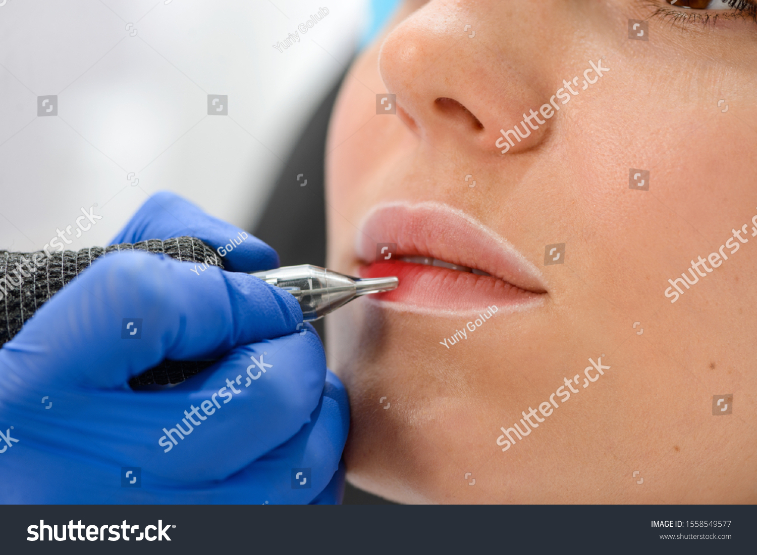 Close up on woman's lips getting a permanent makeup. Cosmetologist using a tattoo machine to tint the lips. #1558549577