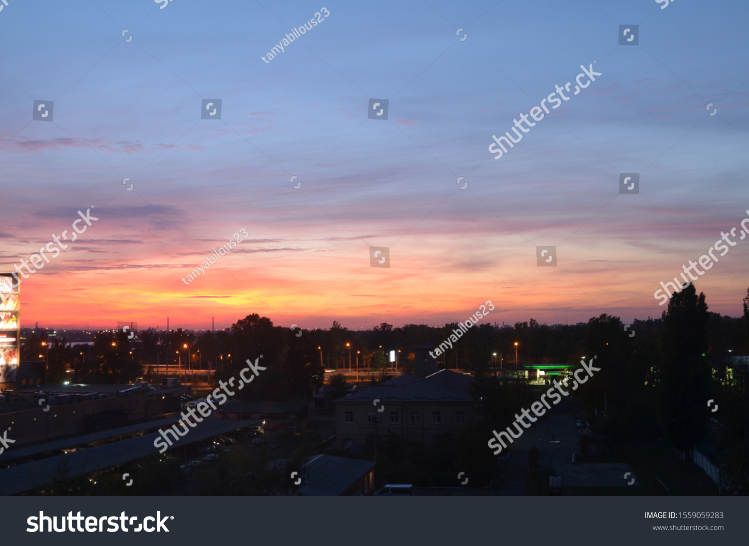 View of the dramatic sky above the sity at sunset with dark blue clouds and pink, purple and yellow flashes from the sun's rays #1559059283