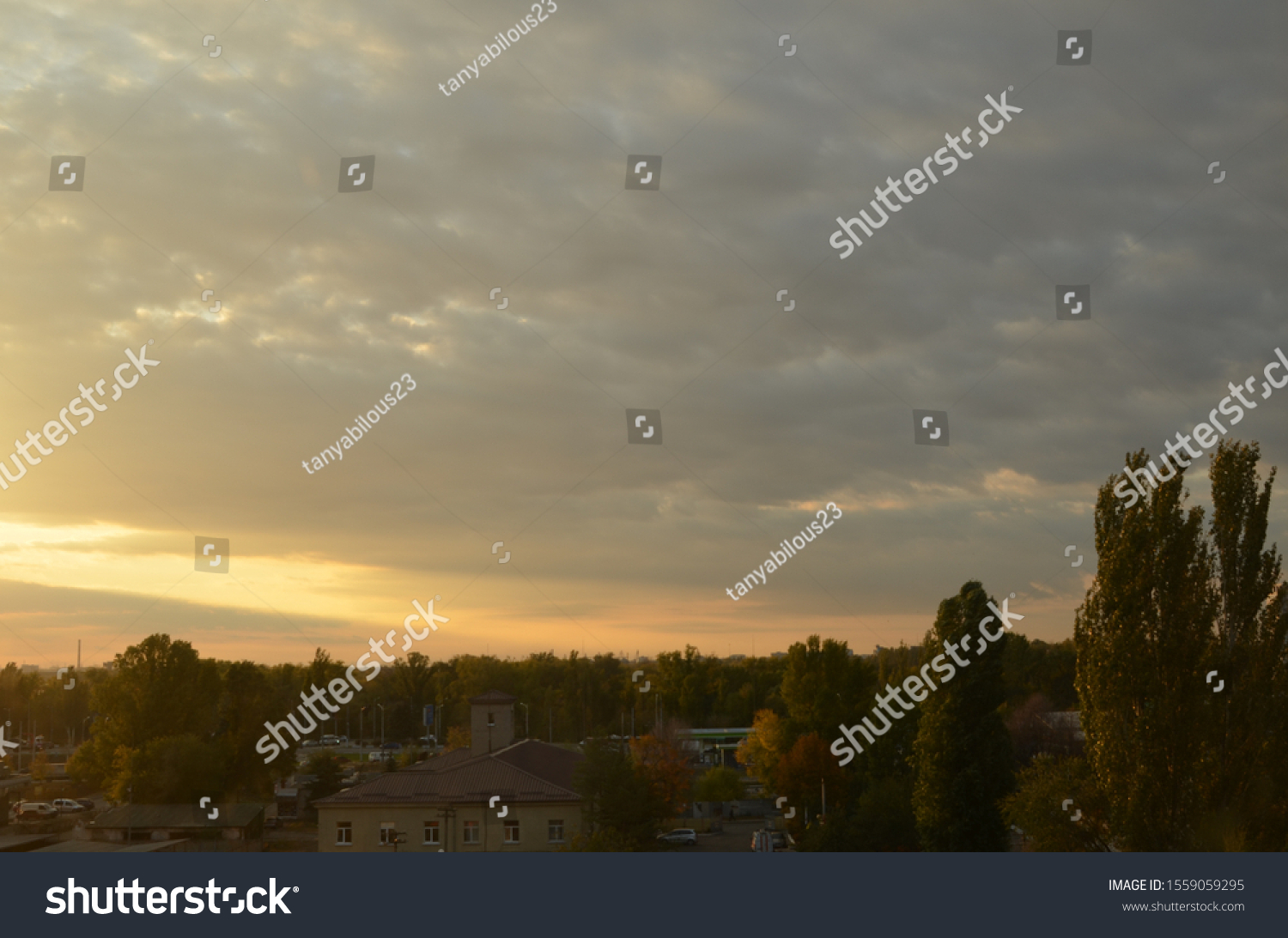 View of the dramatic sky above the sity at sunset with dark blue clouds and pink, purple and yellow flashes from the sun's rays #1559059295