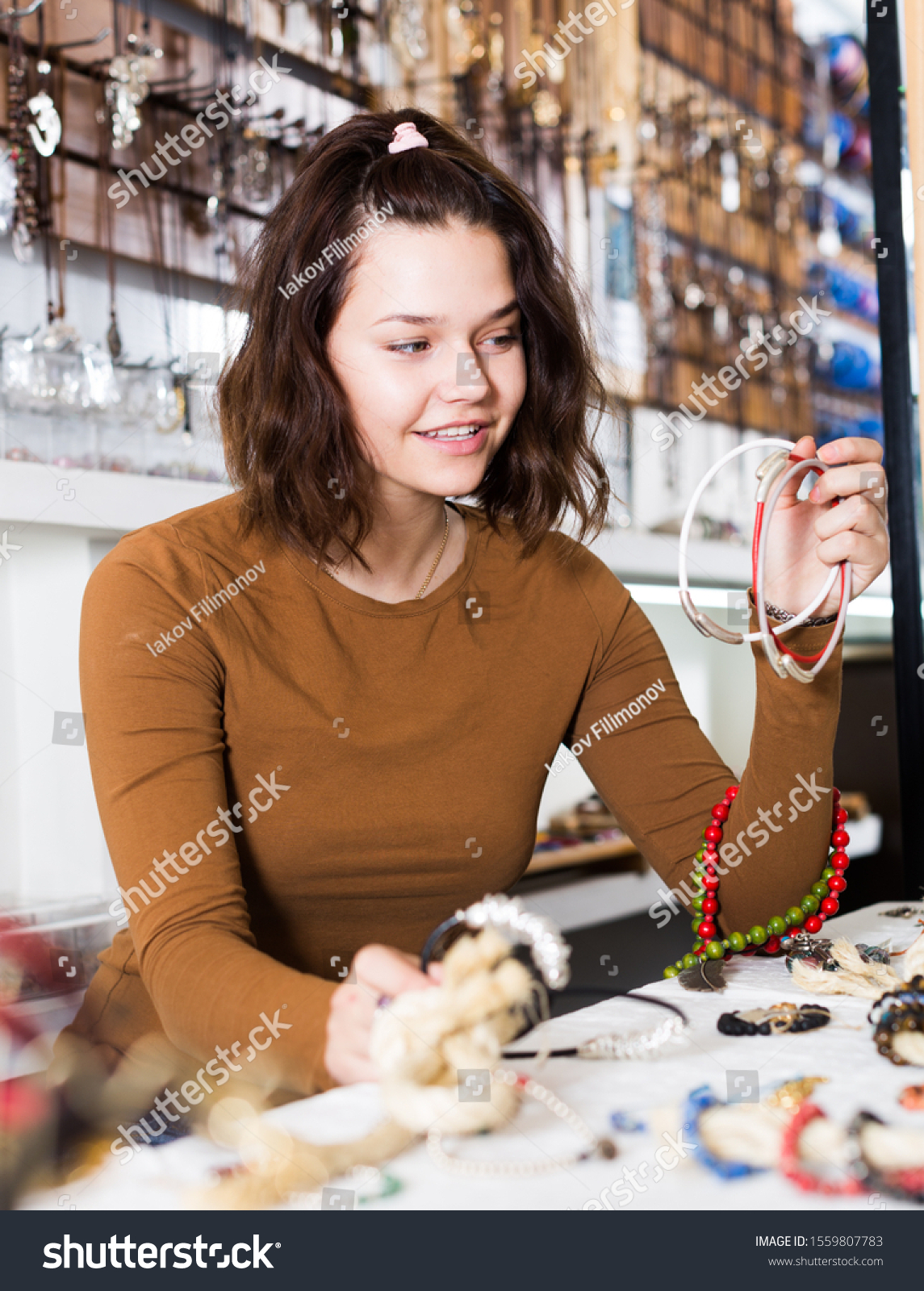 Smiling young woman showing different pendants in the market #1559807783