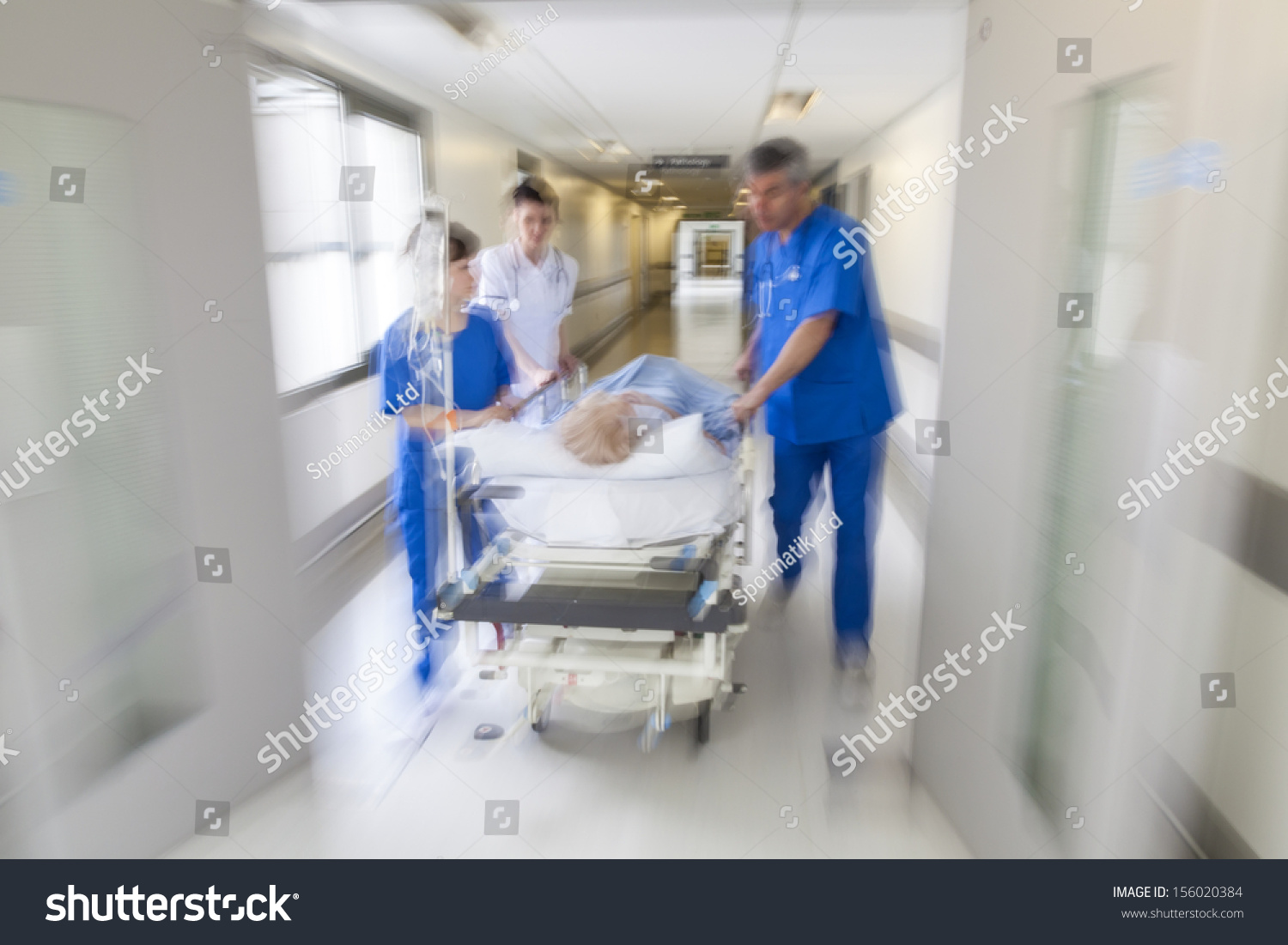 A motion blurred photograph of a patient on stretcher or gurney being pushed at speed through a hospital corridor by doctors & nurses to an emergency room #156020384