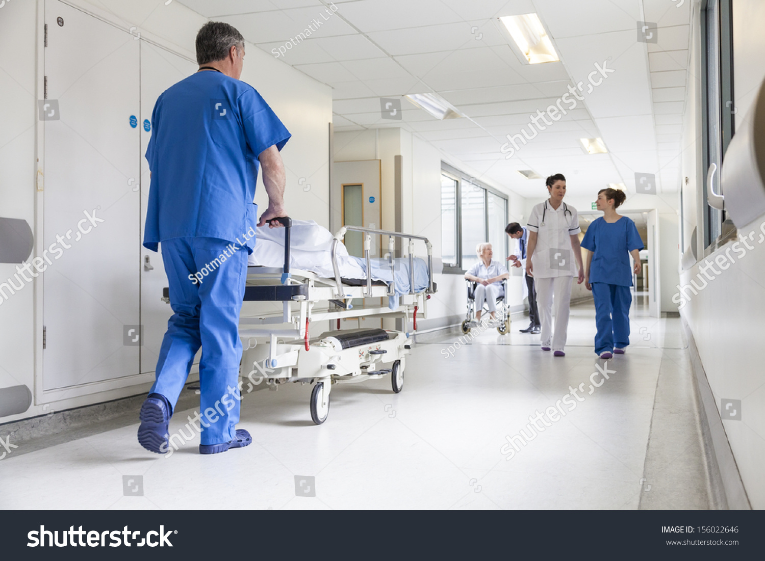 Male nurse pushing stretcher gurney bed in hospital corridor with doctors & senior female patient #156022646
