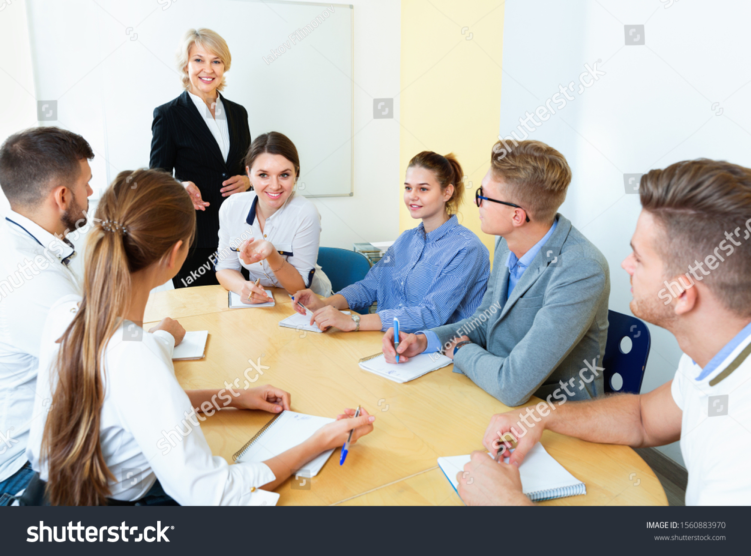 Pleasant female speaker giving presentation for cheerful positive smiling students in lecture hall  #1560883970