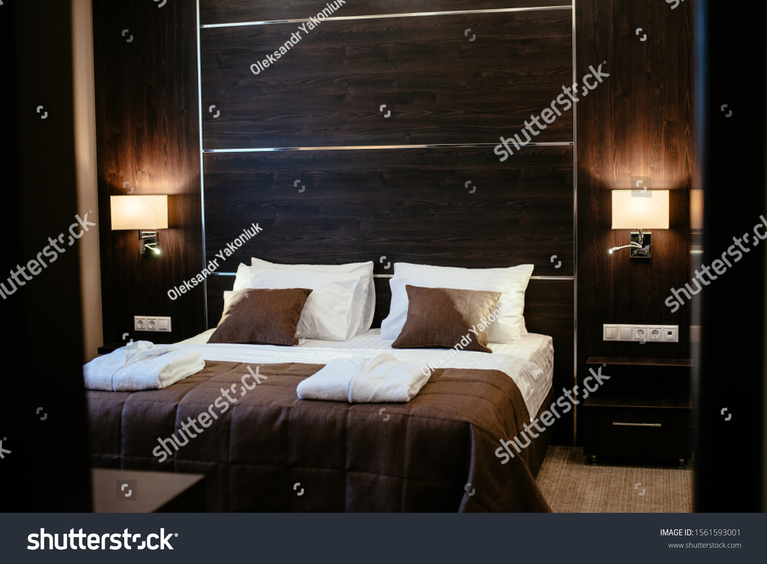 A cozy hotel room in a pastel-brown. Close Up of a large bed with a wooden headboard and beautiful bedding, with pillows and a blanket in brown, white in the modern bedroom interior. Film noise #1561593001