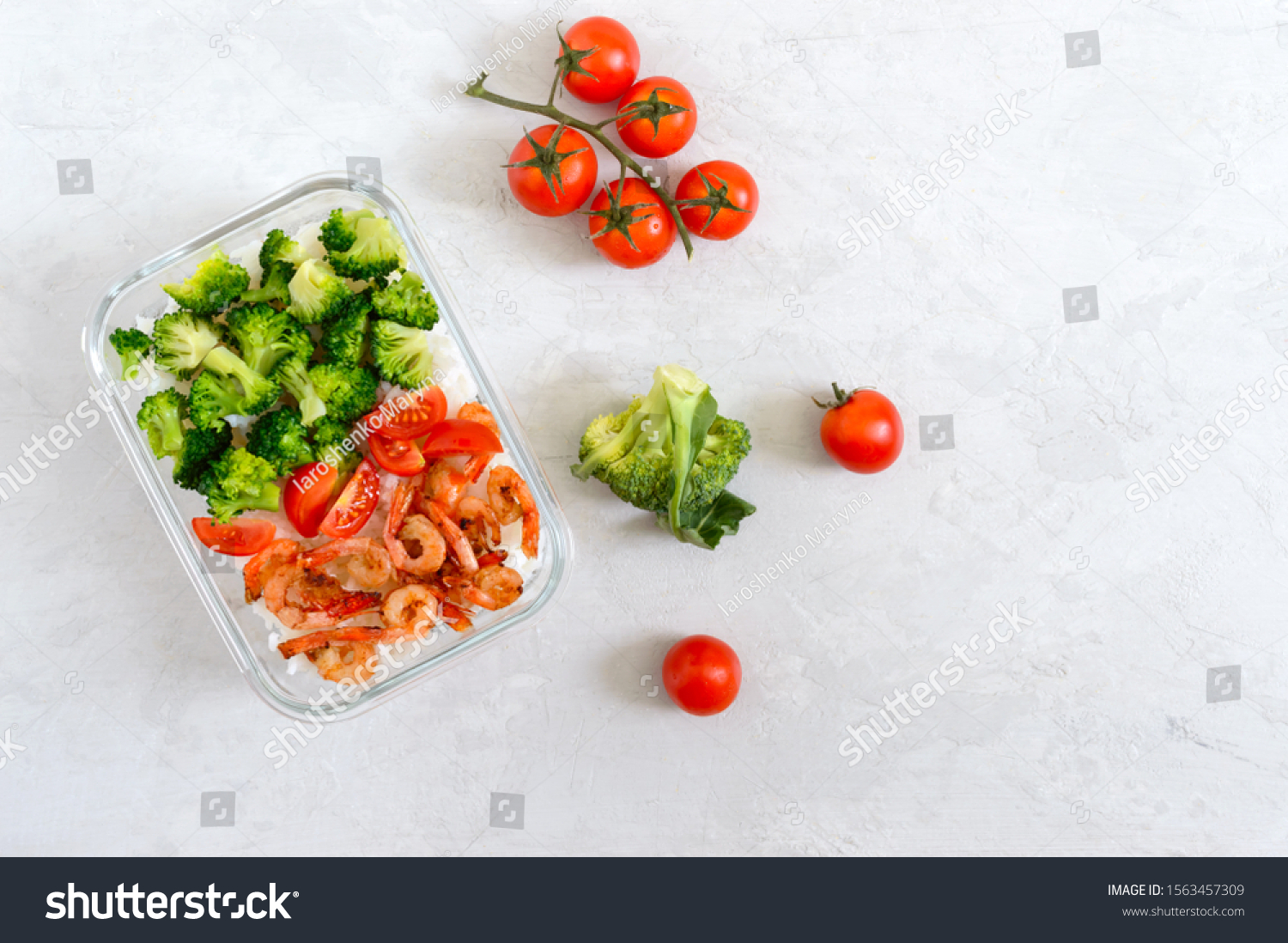 Glass lunch box with a useful lunch on a light background. Rice, broccoli, shrimp, fresh cherry tomatoes - healthy and tasty food. Proper nutrition. Sports diet. Top view #1563457309