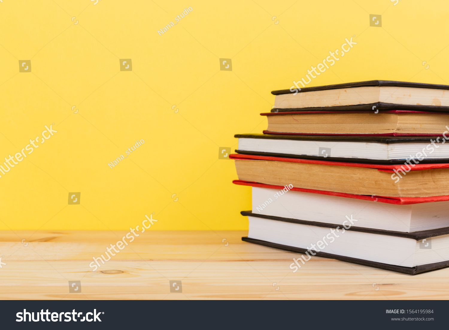 Simple Simple composition of many hardback books, unprocessed books on a wooden table and a yellow background. back to school. Copy space. Education. #1564195984