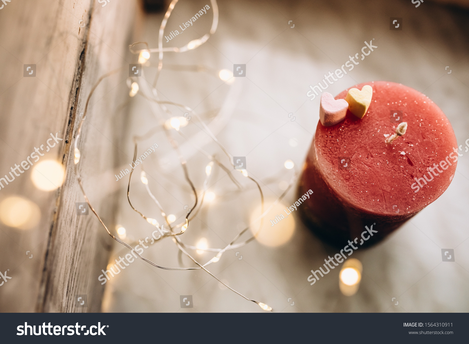 Romantic candle on a bokeh background. On top of the candle are two marshmallow hearts. New Year decorations and decorations #1564310911