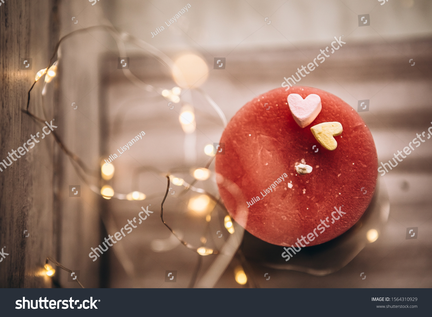 Romantic candle on a bokeh background. On top of the candle are two marshmallow hearts. New Year decorations and decorations #1564310929