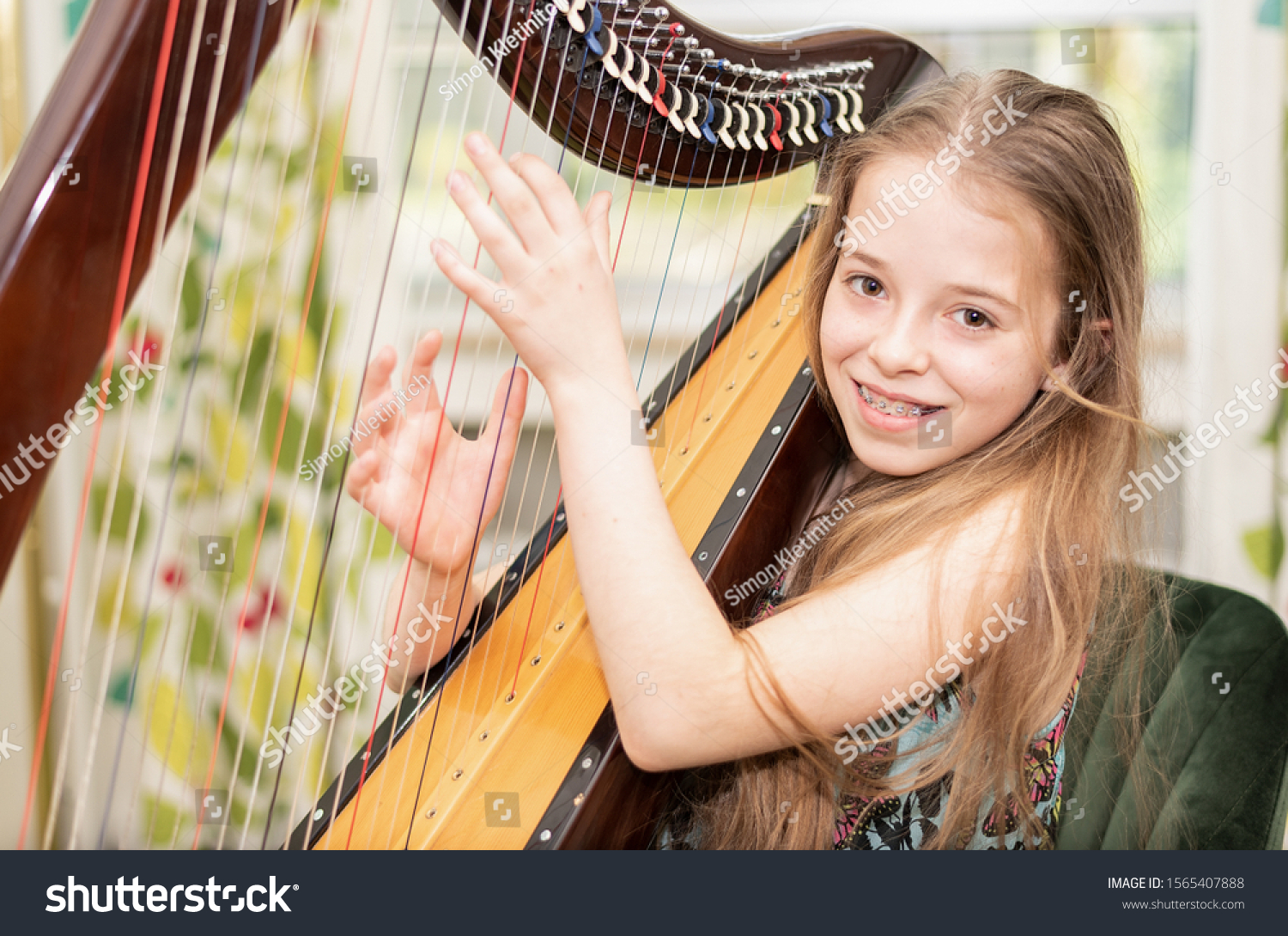 A young girl plays harp and looks at the camera with a smile #1565407888