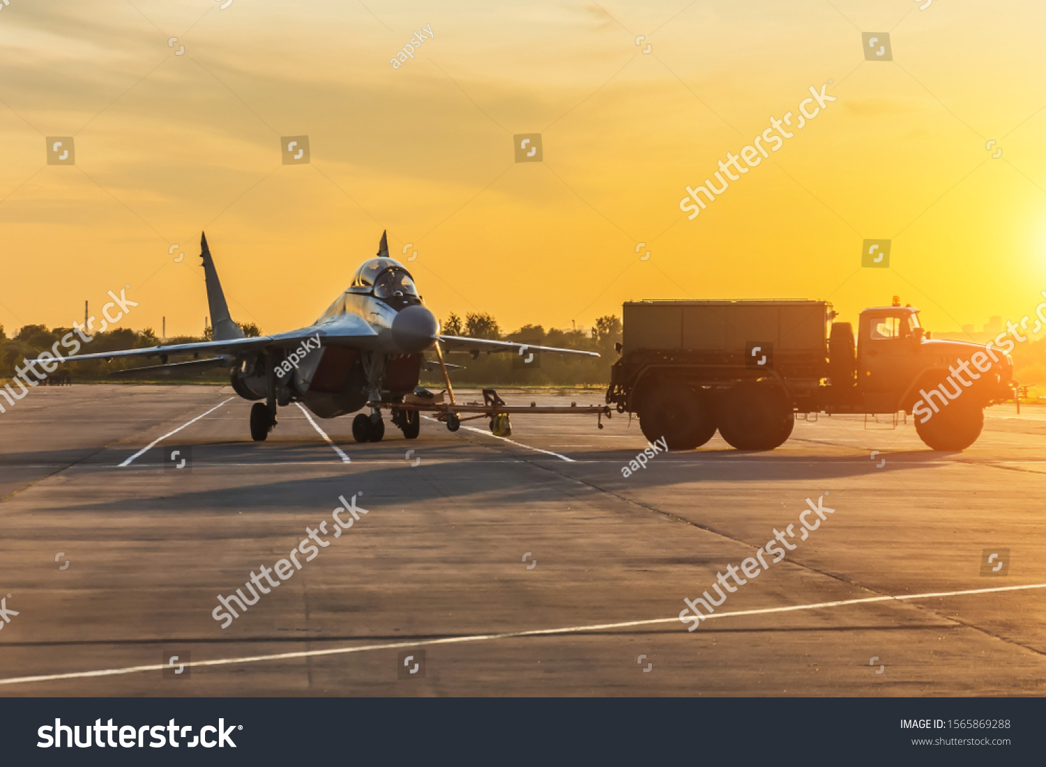 Military fighter is being pushed to a parking lot by a military vehicle at an air base in the evening at sunset #1565869288