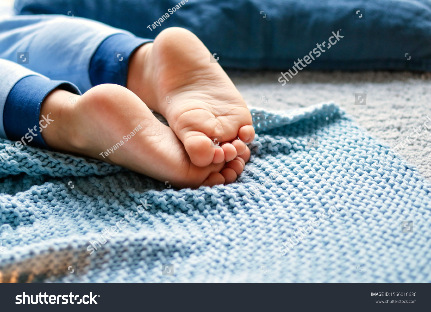 Cozy holidays at home. Close up photo of little child barefooted feet on blue knitted blanket lying on floor in pyjama. Winter season lifestyle. Leisure time. Sweet childhood. Copy space  #1566010636