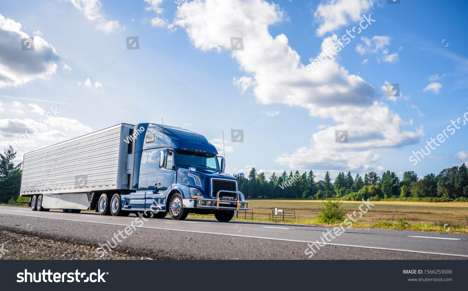 Big rig powerful professional industrial blue bonnet semi truck for long haul delivery commercial cargo going with refrigerator semi trailer on the summer road with forest and meadows on the sides #1566259006