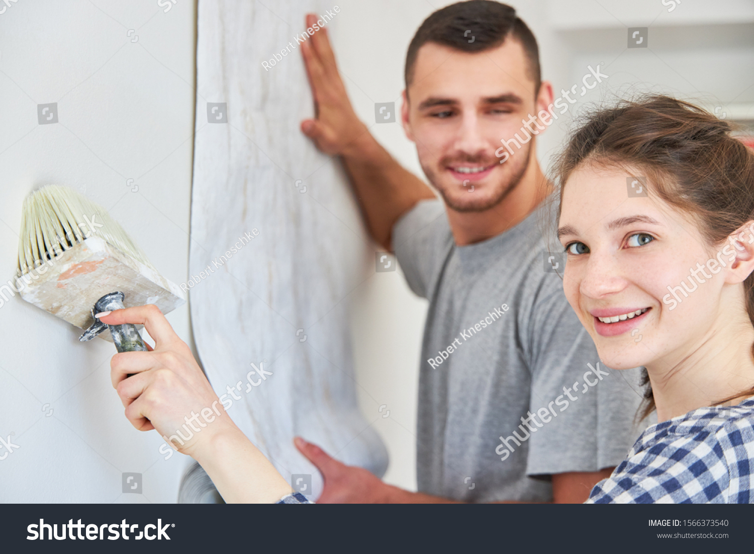 Young woman renovating with paste brush while wallpapering with wallpaper on a wall #1566373540