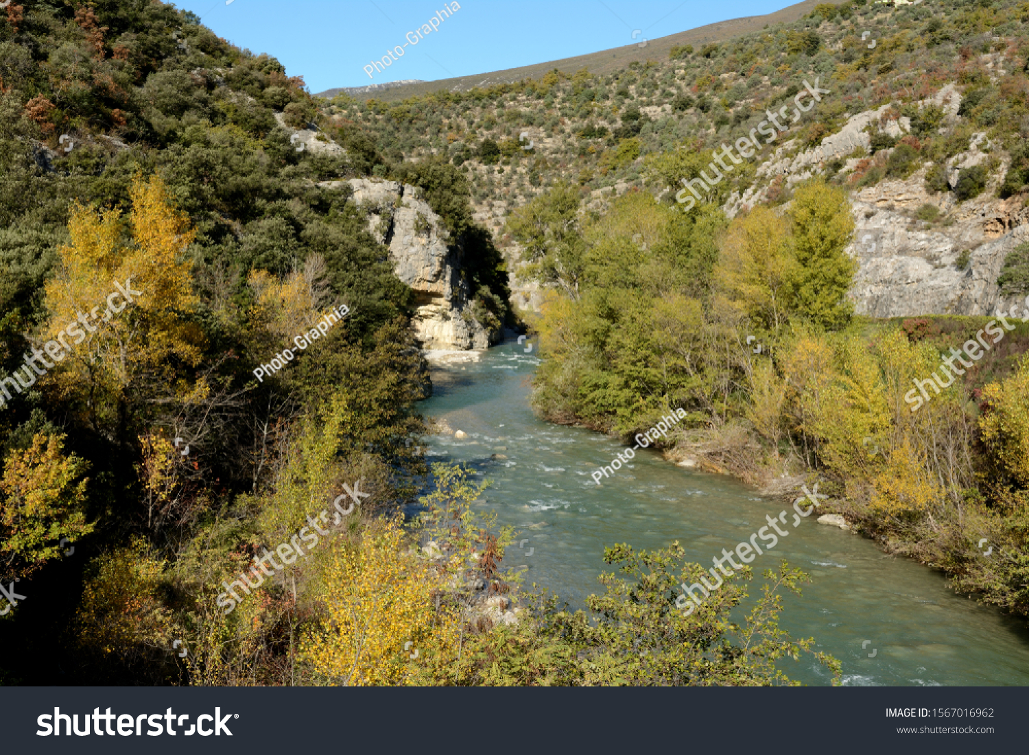 A river flows between mountains in South France, it turns right, it turns left. Trees with autumnal colours. #1567016962