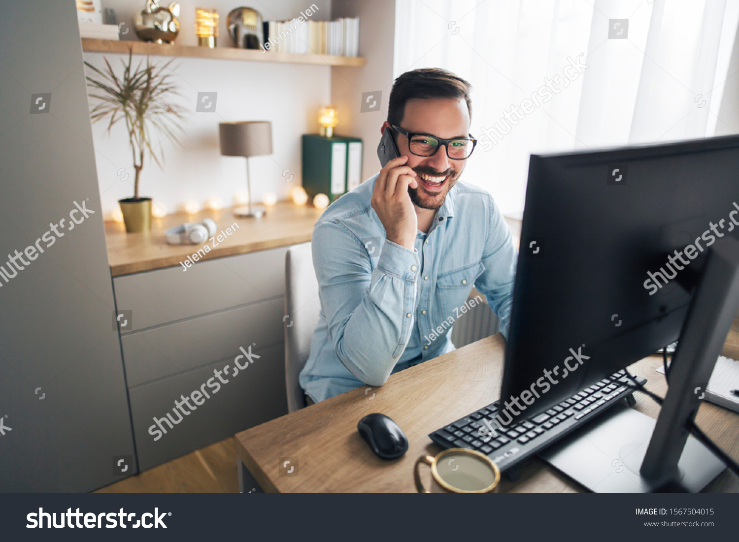Smiling handsome freelancer working remotely from home. He is speaking on the phone. #1567504015