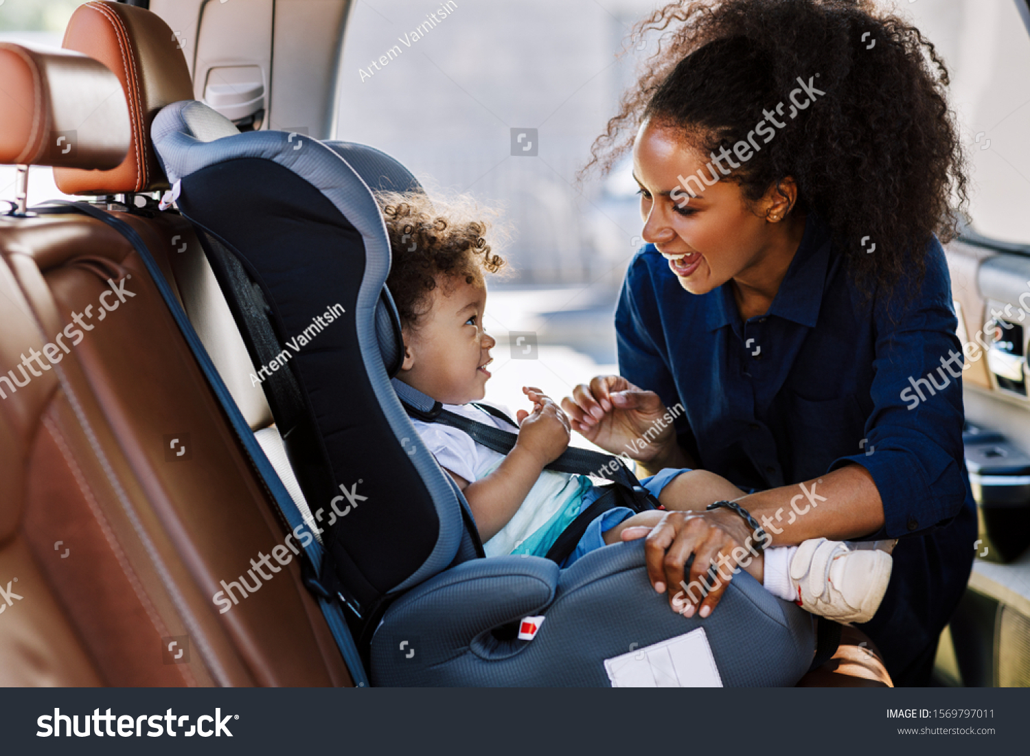 Happy mother looking at her son in a baby seat. Young female preparing kid for a trip. #1569797011