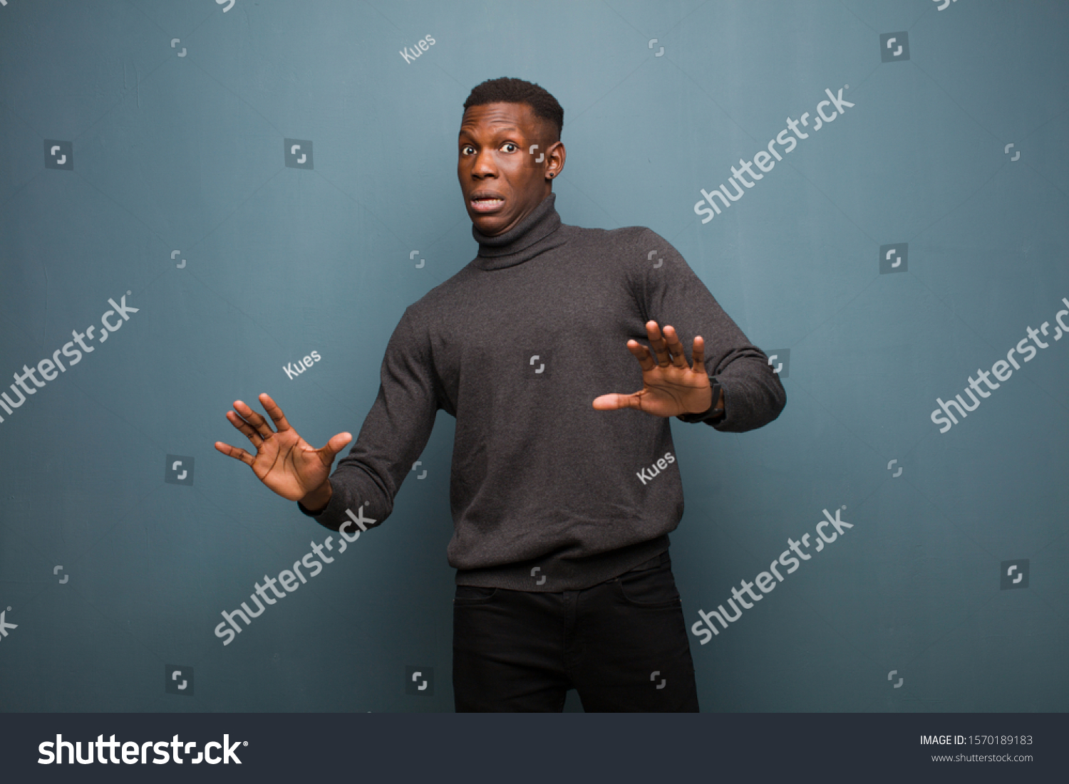 young african american black man feeling stupefied and scared, fearing something frightening, with hands open up front saying stay away against grunge wall #1570189183