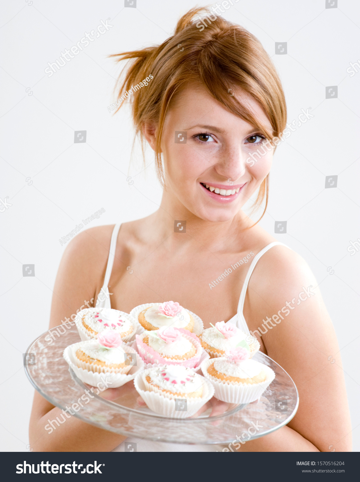 Portrait of young woman holding platter of cupcakes, studio shot #1570516204