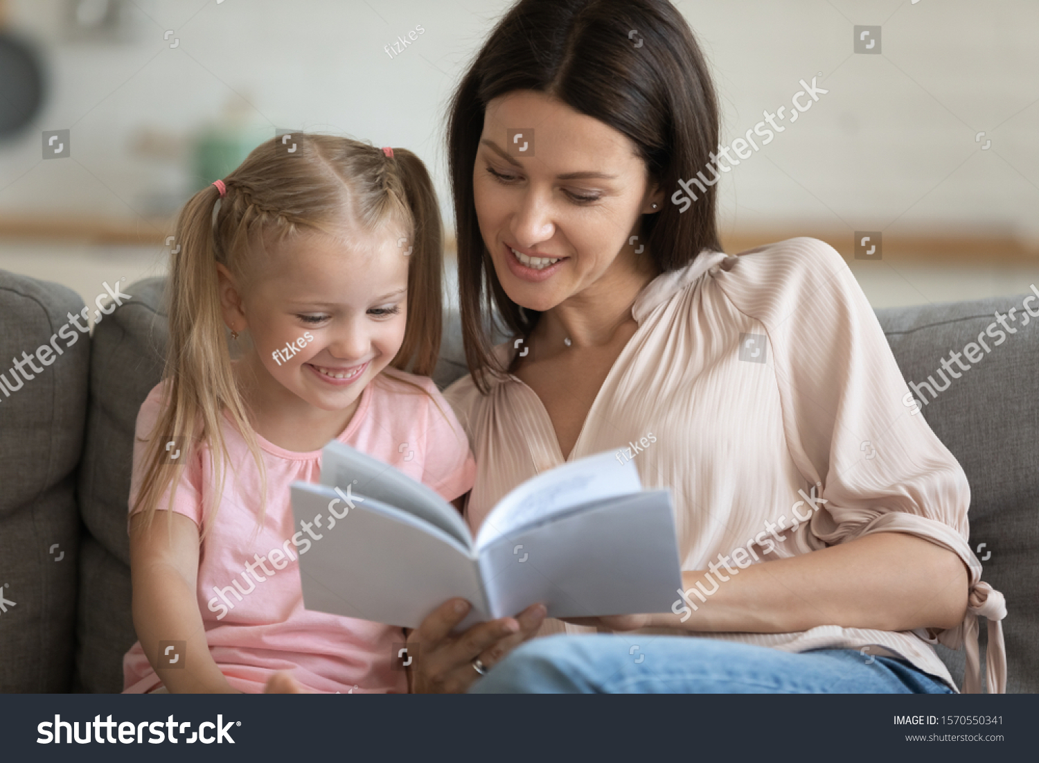 Caring single parent young adult mother and happy cute little preschool child daughter reading book learning education fairy tale story bonding enjoying family lifestyle hobby at home sit on sofa #1570550341
