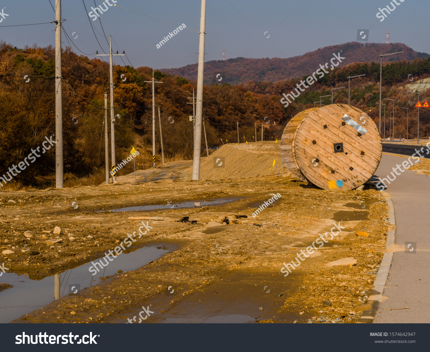 Large wooden industrial spools sitting on ground next to sidewalk of paved road. #1574642947
